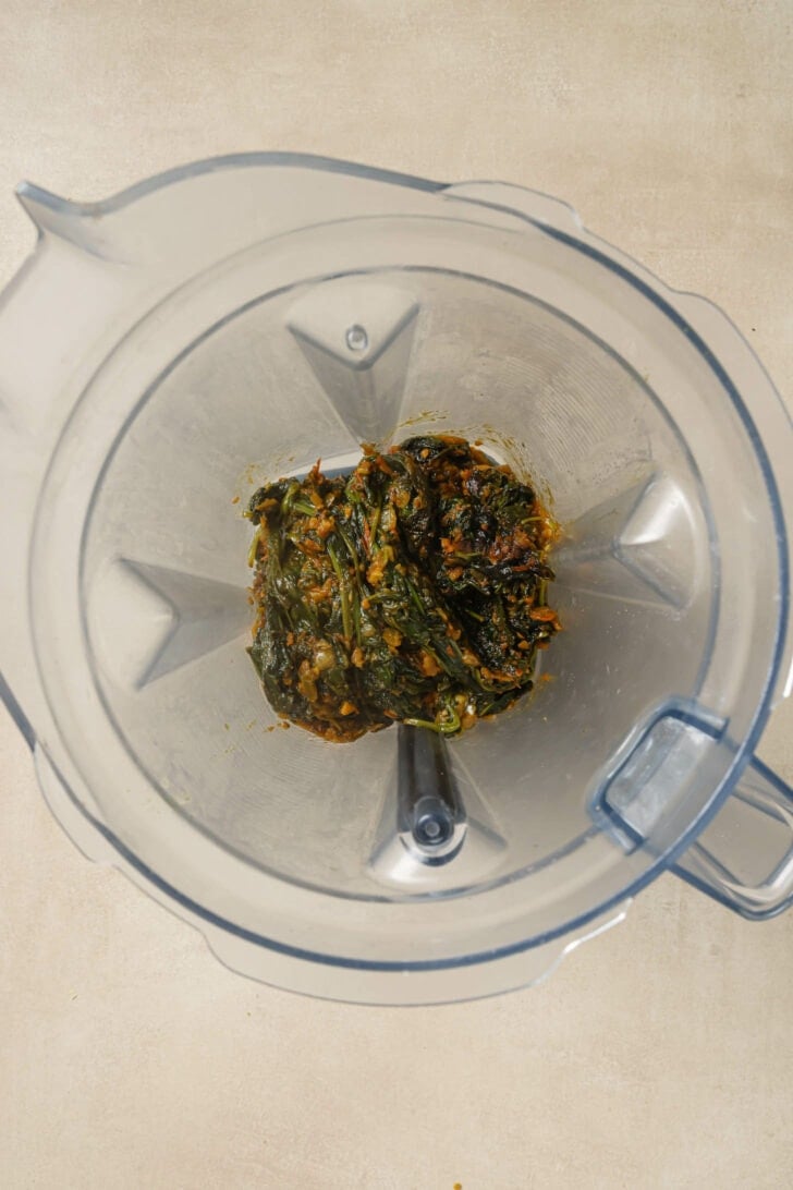 Cooked spinach and tomato mixture added to a blender.