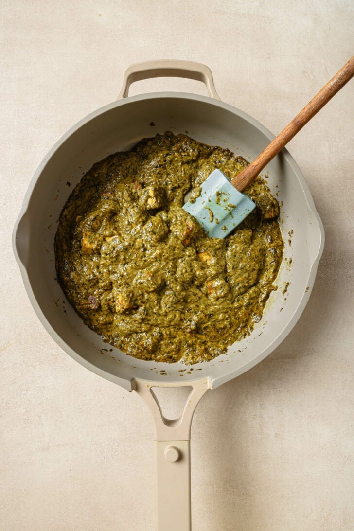 Palak Paneer in a pot with a rubber spatula.