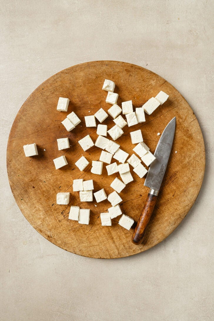 Cubed paneer on a wooden cutting board with a knife.