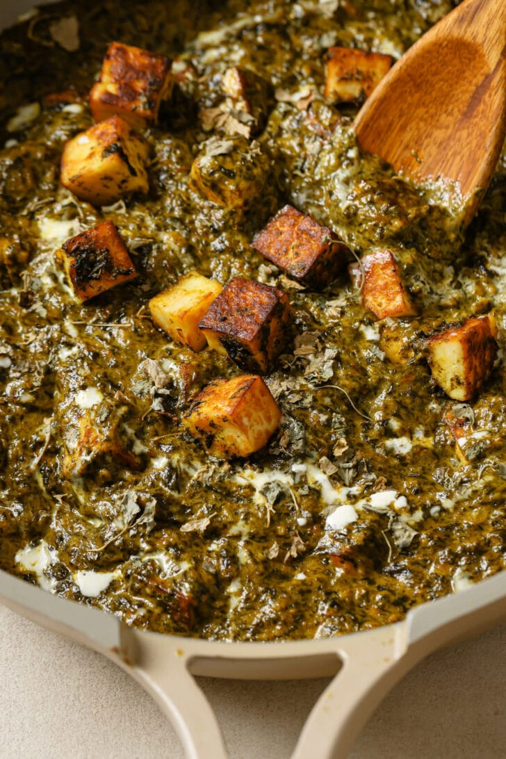 Close up of Palak Paneer in a pot with a wooden spoon.