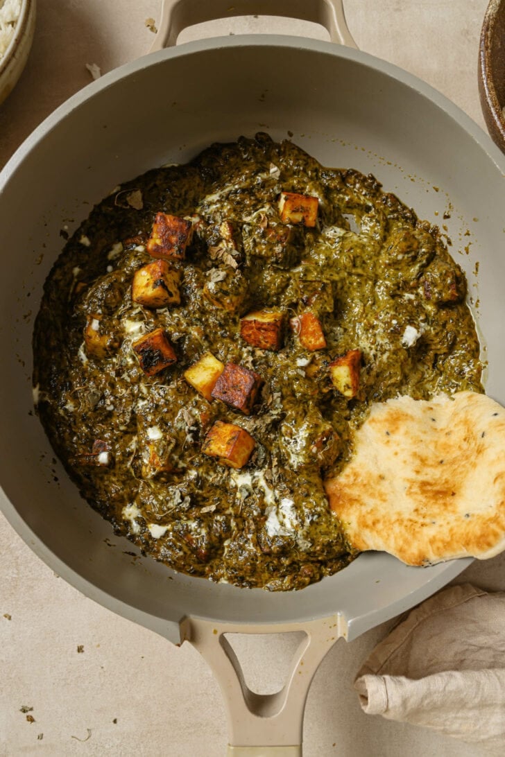 Top view of Palak Paneer in a pot with a piece of naan dipped in.