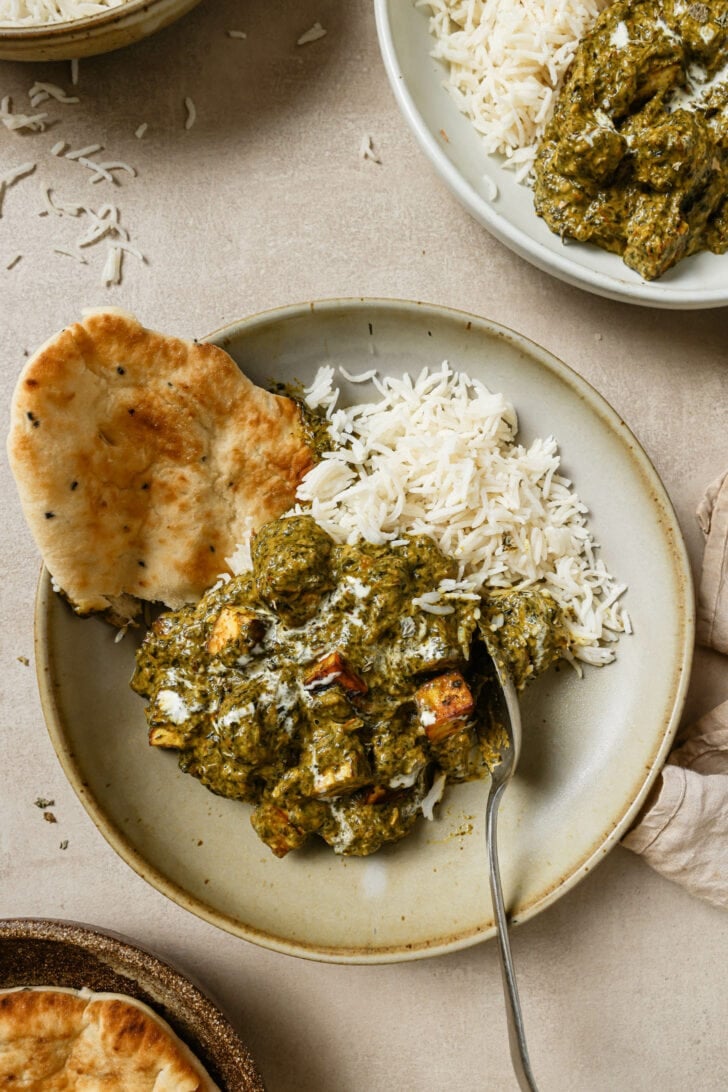 Palak Paneer on a round plate with rice and naan ready to be eaten.
