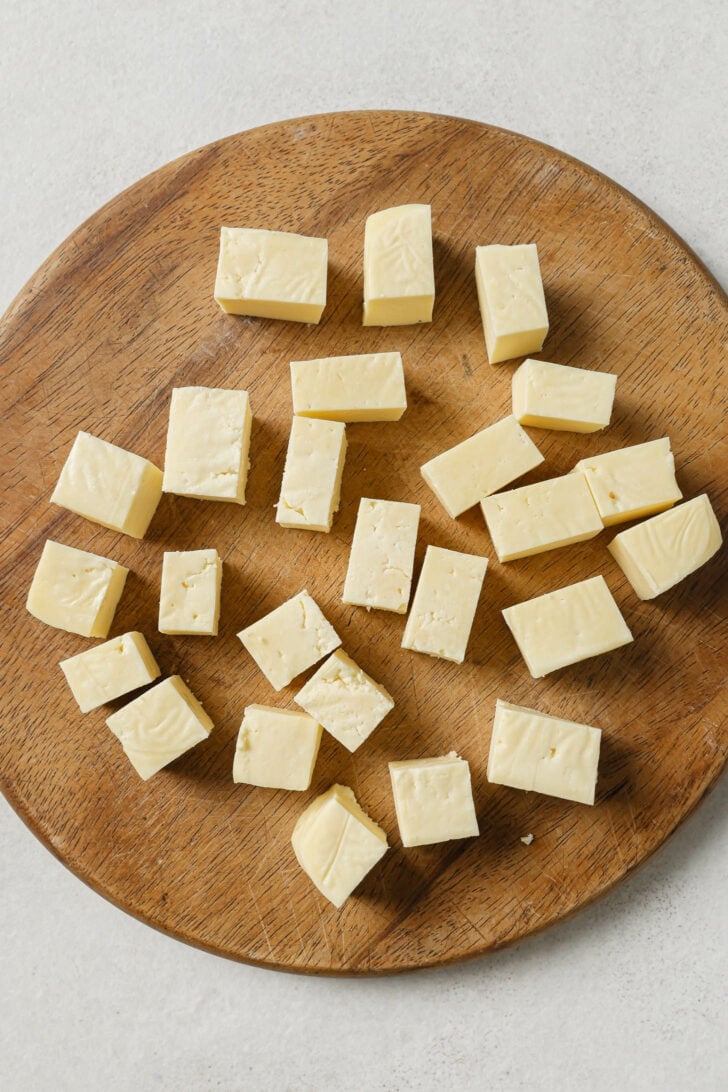 Cubed paneer on a wooden cutting board.