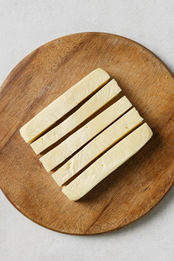 Paneer cut into 1/2" vertical strips on a wooden cutting board.