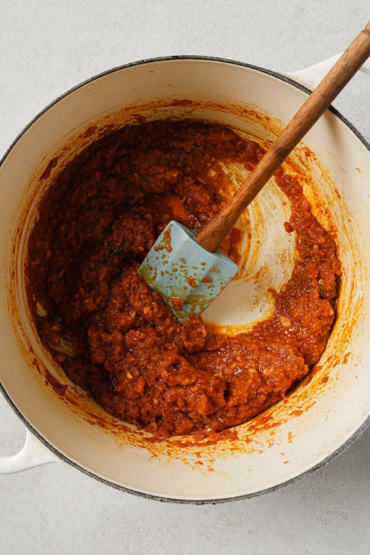 Cooking onion mixture, tomato paste, puréed tomatoes, green chili and ground spices in a dutch oven with a rubber spatula.