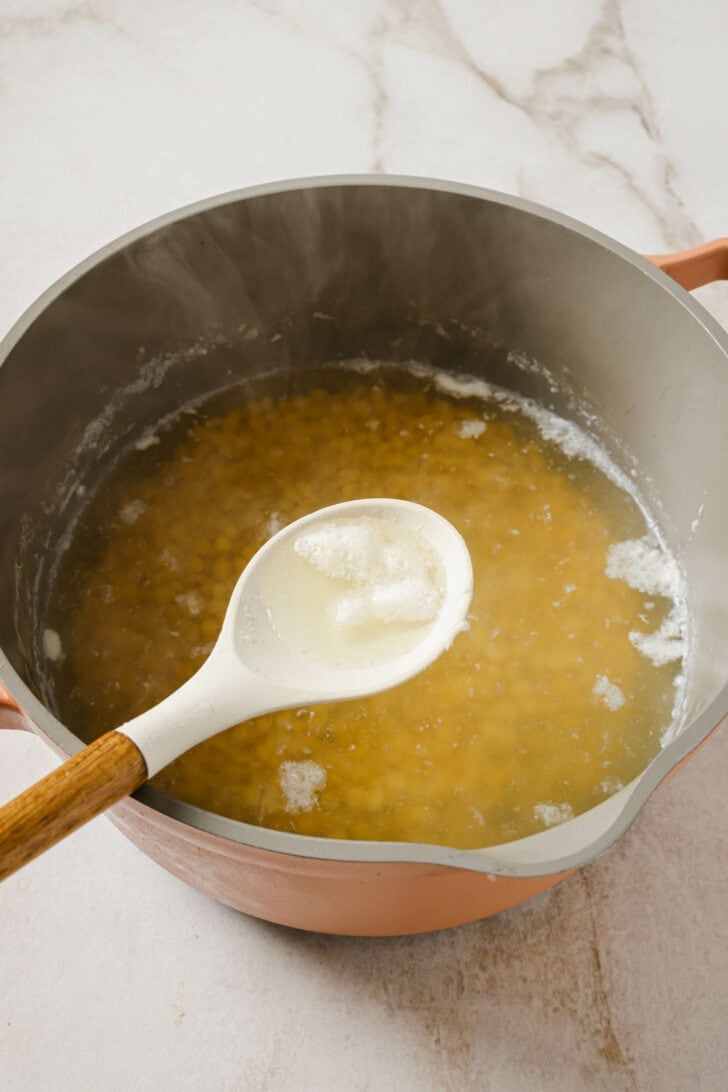 Using a spoon to remove scum from a pot that has emerged from boiling Chana Dal.