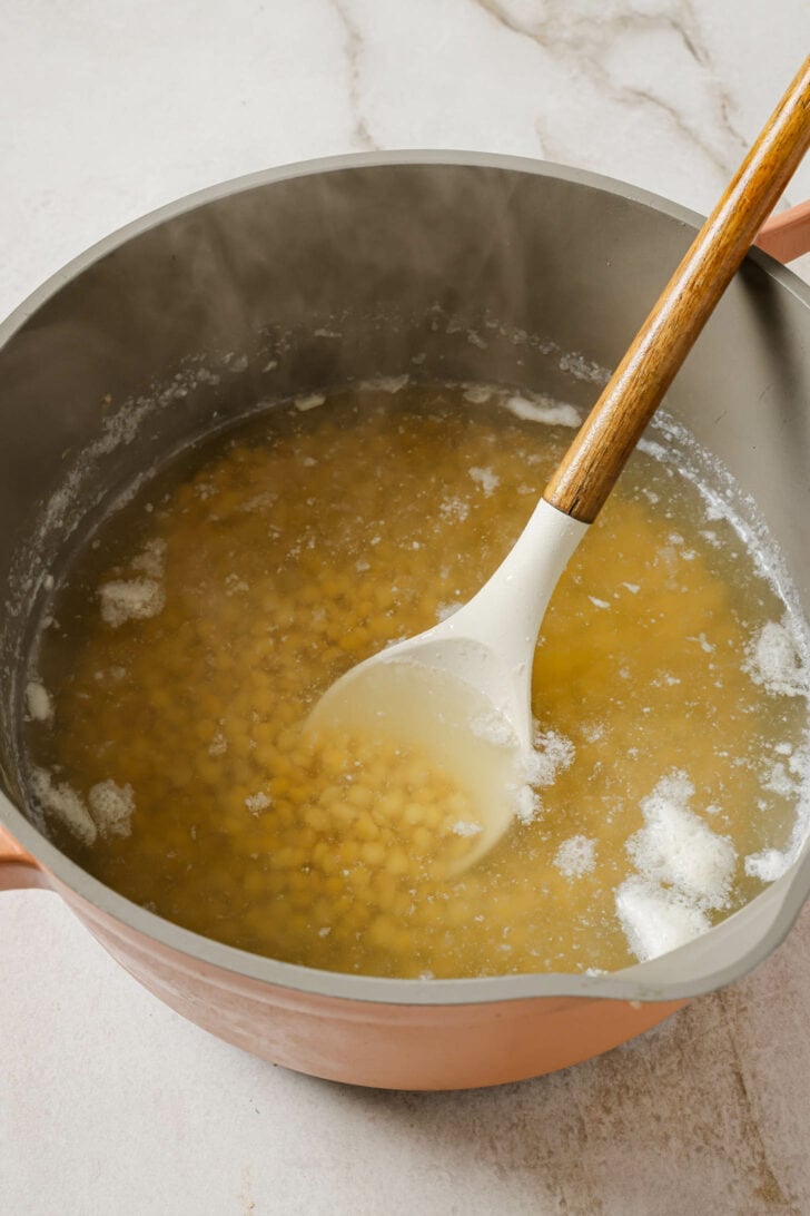 Using a spoon to remove scum from a pot that has emerged from boiling Chana Dal.