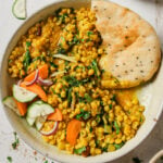 Chana Dal in a bowl garnished with sliced vegetables, sliced green chili, julienned ginger and cilantro with naan on the side.