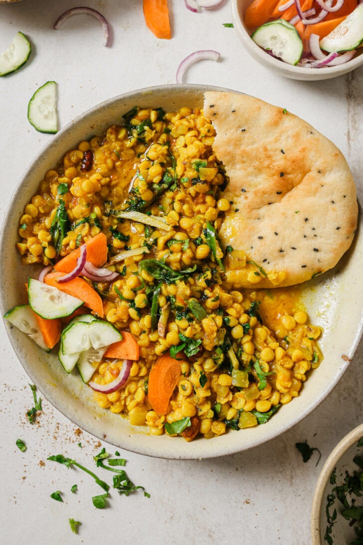 Chana Dal in a bowl garnished with sliced vegetables, sliced green chili, julienned ginger and cilantro with naan on the side.