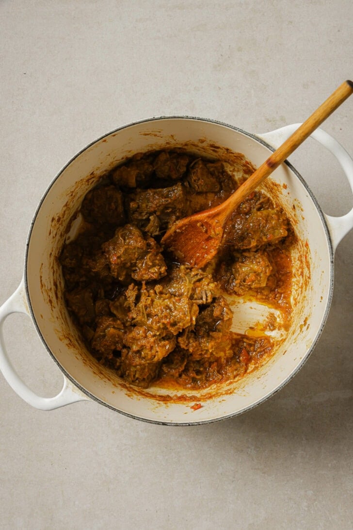 Cooked goat/lamb in a dutch oven with a wooden spoon.