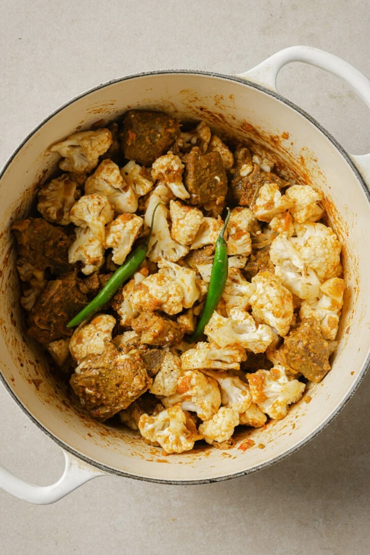 Chopped cauliflower and whole green chilies added to dutch oven with the cooked goat/lamb masala.