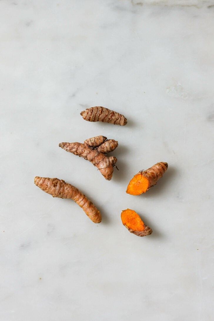 Fresh turmeric root on a marble surface with one cut open.