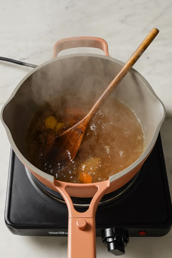 Simmer water, ginger, turmeric and black pepper in a pot with a wooden spoon to make Turmeric Tea.