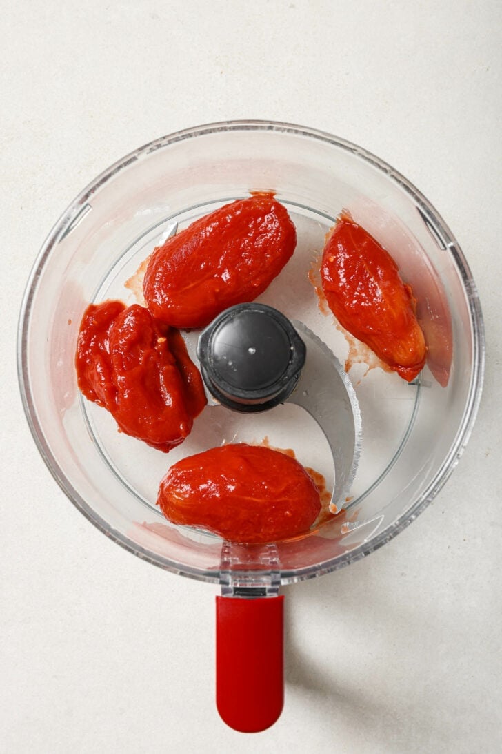 Drained whole tomatoes in a food processor ready to be puréed.