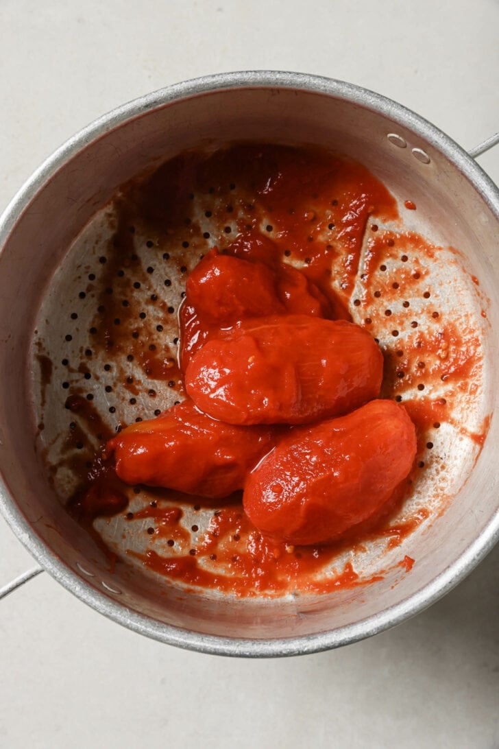 Drained canned whole tomatoes in a strainer.