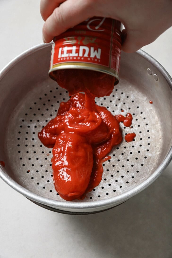 Draining liquid from a can of tomatoes.