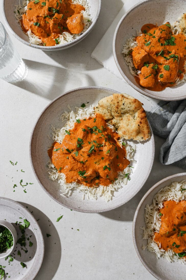Bowls of Butter Chicken a top of rice with naan on the side.
