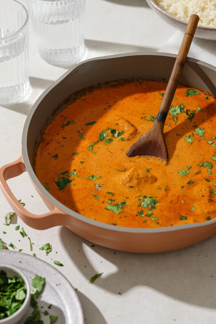 Butter Chicken in a skillet garnished with cilantro on a dinner table.
