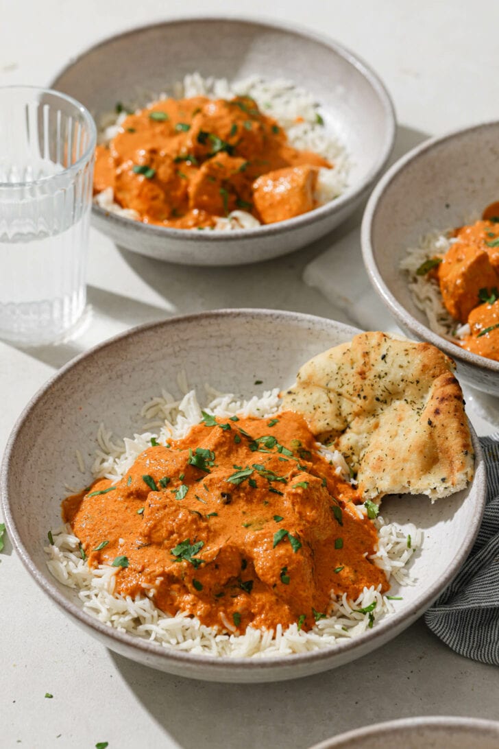 Bowls of Butter Chicken a top of rice with naan on the side.