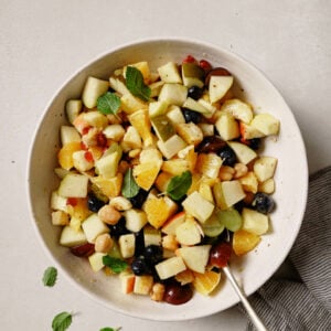 Fruit Chaat in a bowl with a spoon garnished with mint leaves.