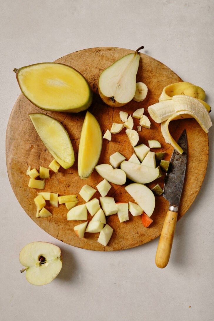 Chopped fruit on a round wooden cutting board to make Fruit Chaat.