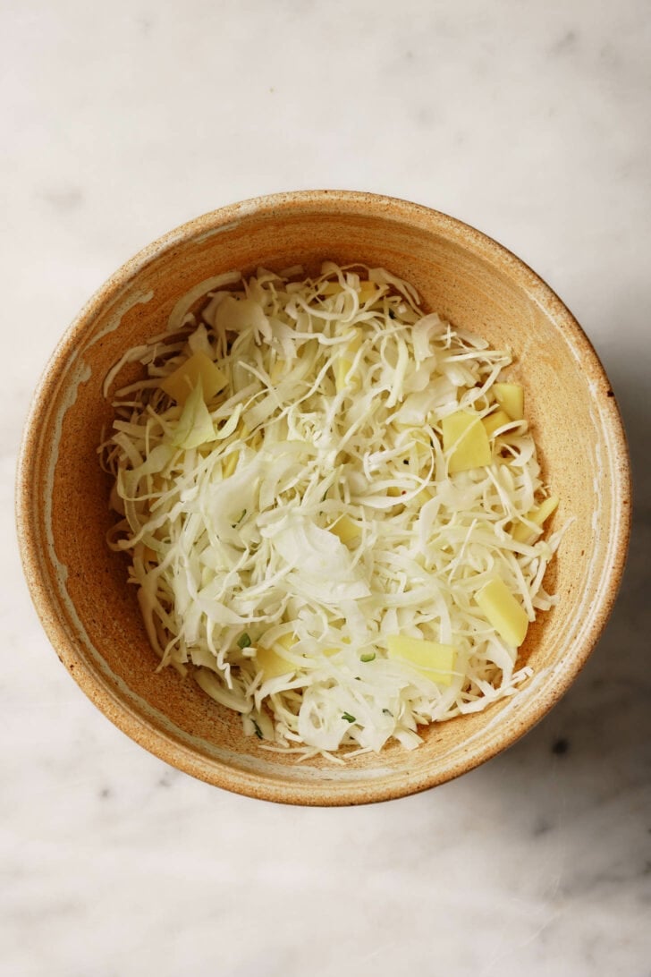 Sliced cabbage, onion and potato mixed in a bowl.