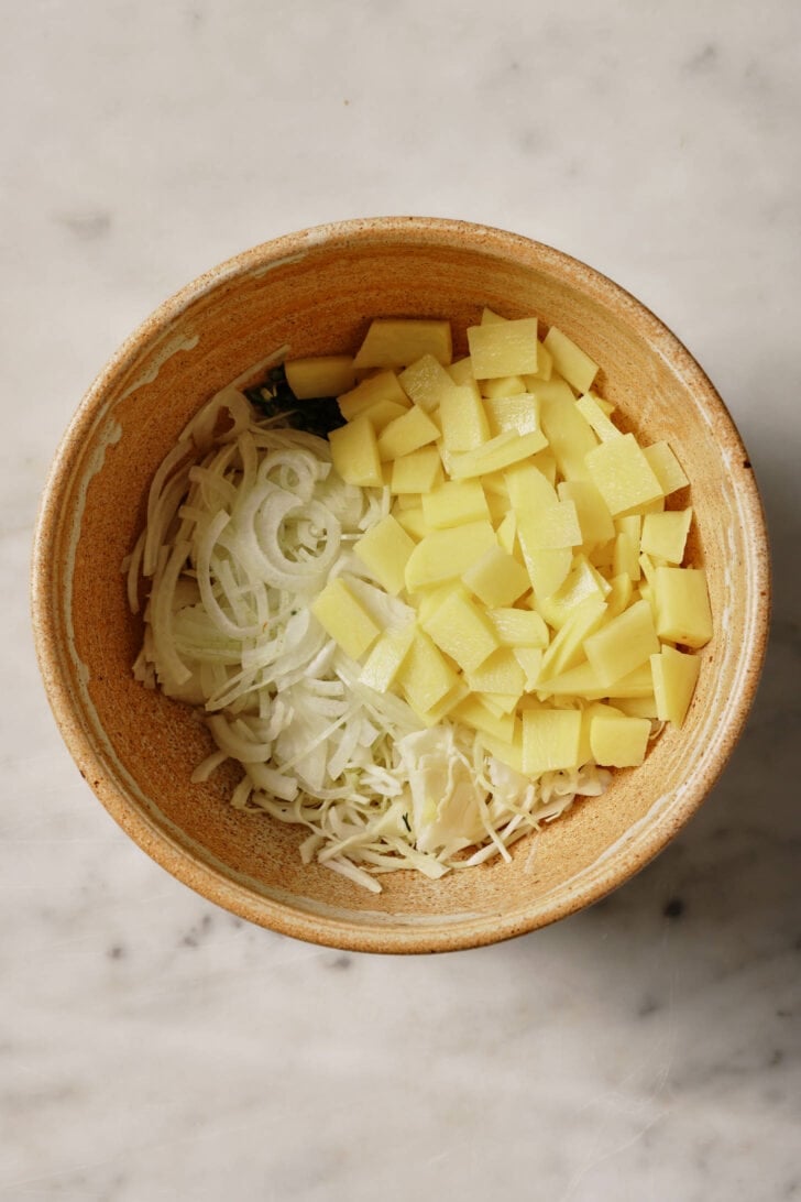 Sliced onions, cabbage and potato in a bowl.
