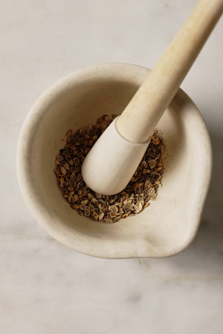 Coriander and cumin seeds crushed in mortar and pestle.
