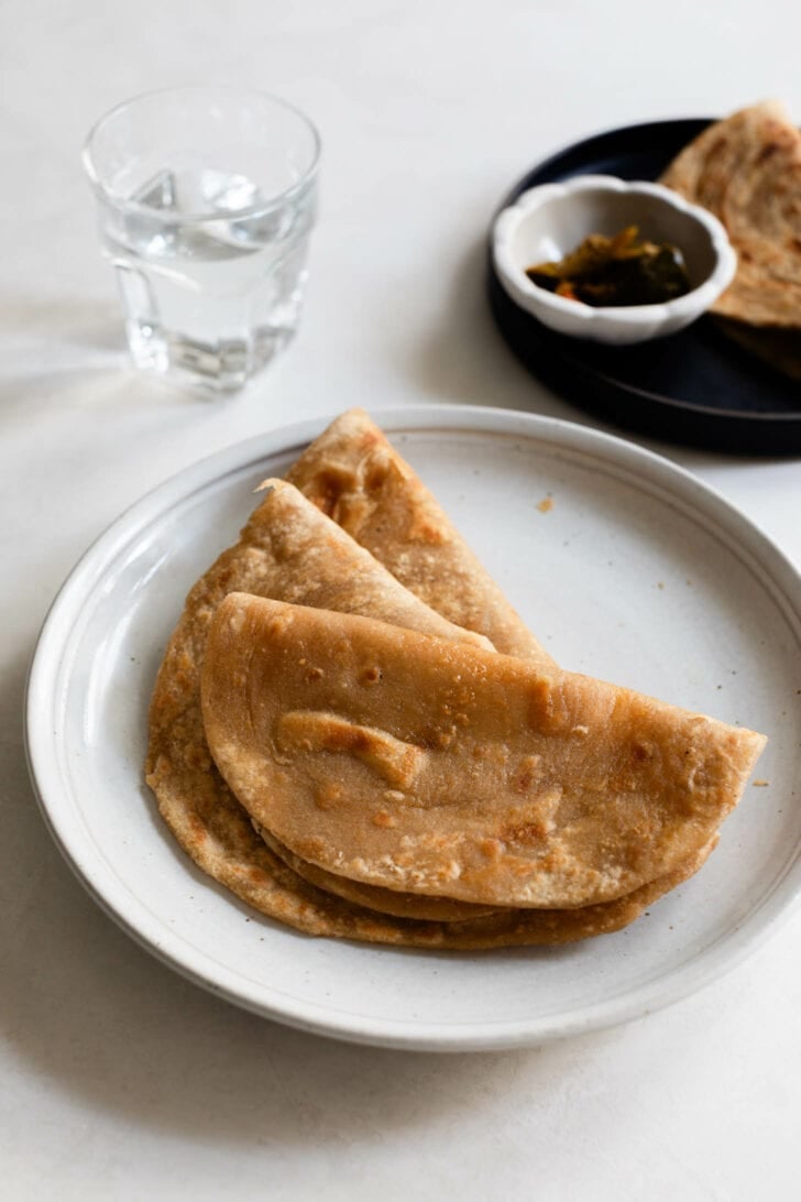 Three parathas folded in half and stacked on a plate.