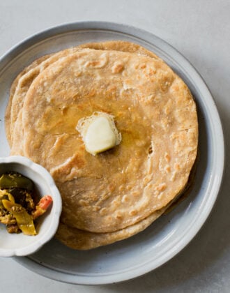 A stack of paratha with a dollop of butter on top alongside a bowl of achaar.