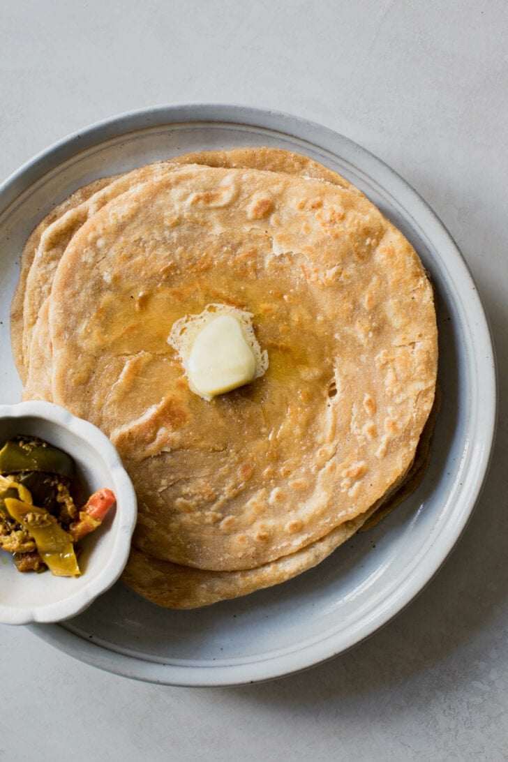 A stack of lachha parathas with a dollop of butter on top alongside a bowl of achaar.