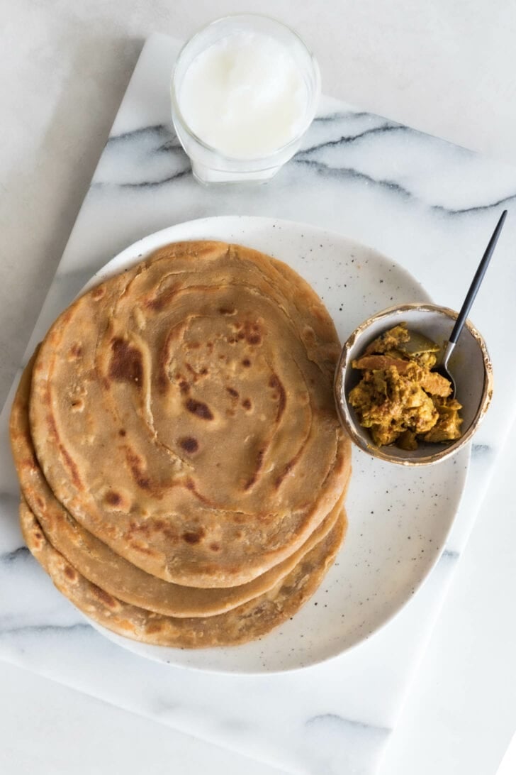 A plate of three paratha with a bowl of achaar on the side.